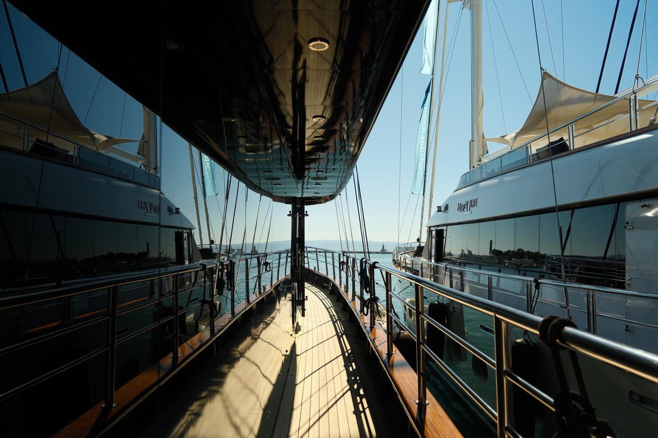 Side deck between two superyachts in a harbour, the hulls reflecting sky and water