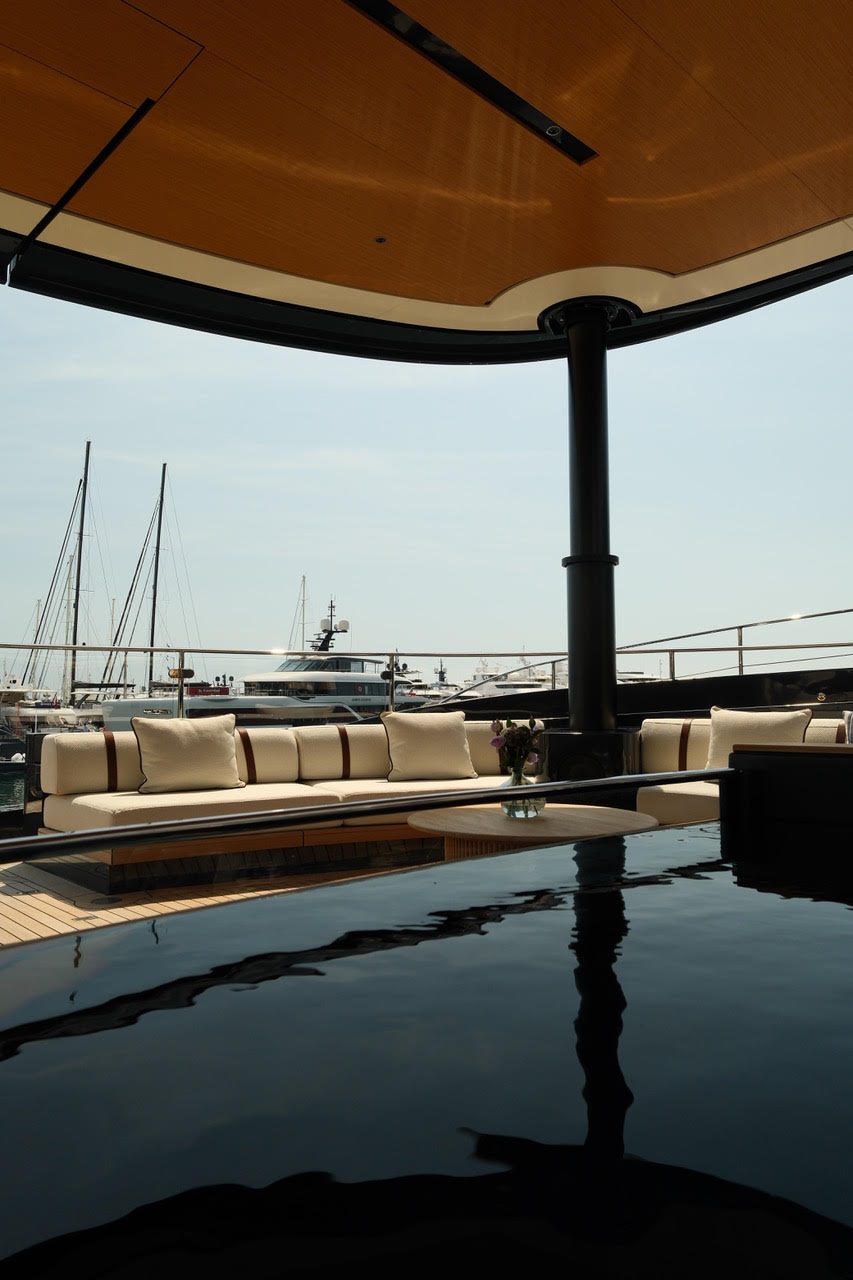 Lounge beneath a wooden canopy on deck, with a dark pool and its reflection in front