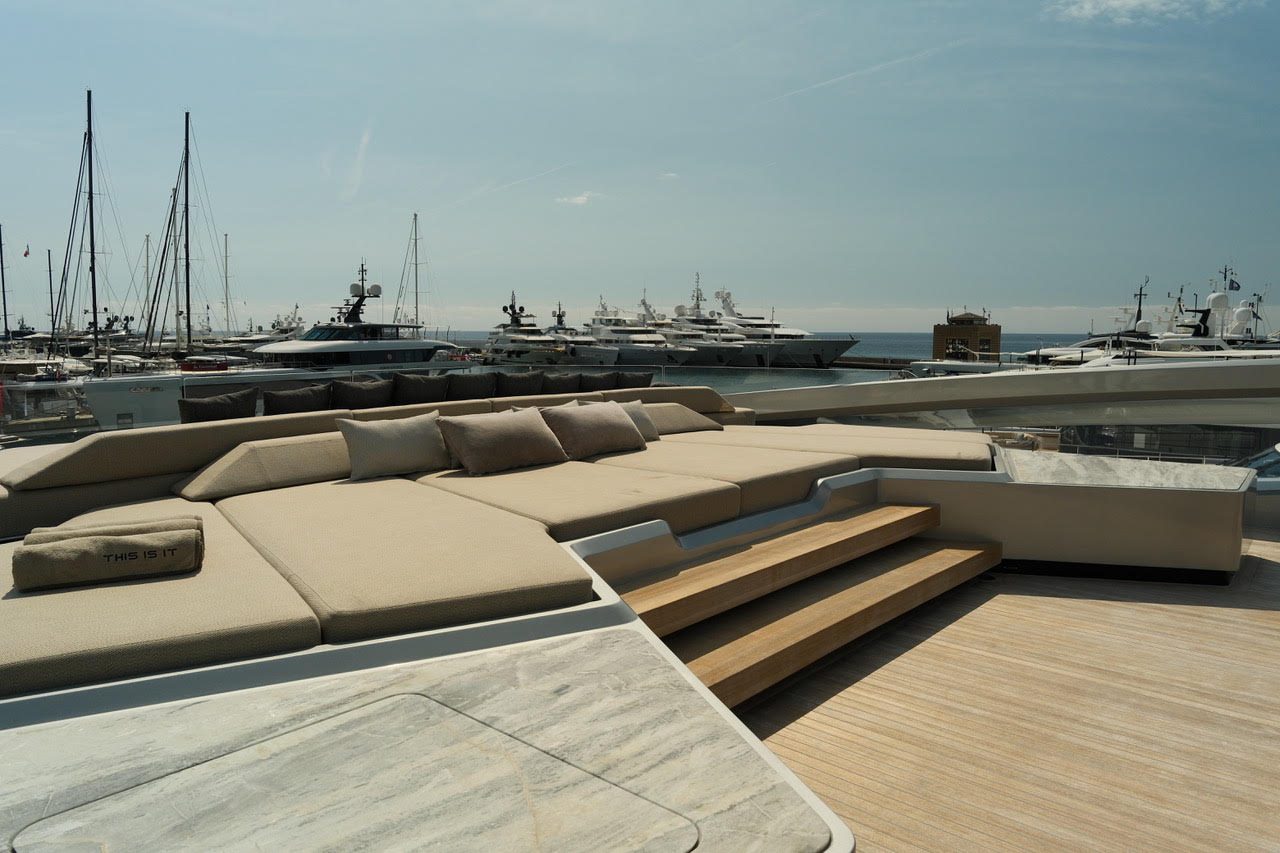 Sun deck of a yacht with a large sunbed, superyachts in the harbour behind